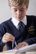 Photo: Close up of male student in school uniform using drawing compass at desk in classroom Close up of male student in school uniform using drawing compass at desk in classroom