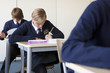 Photo: Students in school uniforms taking exam at desk in classroom Students in school uniforms taking exam at desk in classroom