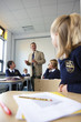 Photo: Students in school uniforms at desks watching and listening to teacher in classroom Students in school uniforms at desks watching and listening to teacher in classroom