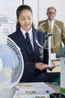 Photo: Teacher in background watching female student in school uniform with wind turbine model in science class Teacher in background watching female student in school uniform with wind turbine model in science class