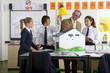 Foto: Teacher and students in school uniforms adjusting lamp over solar panels on house model in science class Teacher and students in school uniforms adjusting lamp over solar panels on house model in science class