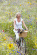 Smiling woman riding bicycle on path through field of wildflowers