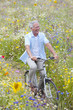 Smiling senior man riding bicycle on path through field of wildflowers