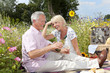 Smiling senior couple drinking wine and having picnic in field of wildflowers
