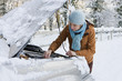 Photo: Woman standing in snow checking underneath carճ hood Woman standing in snow checking underneath carճ hood