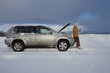 Photo: Woman standing in snow checking underneath carճ hood and talking on cell phone Woman standing in snow checking underneath carճ hood and talking on cell phone