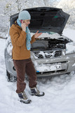 Photo : Woman standing in snow checking underneath carճ hood and talking on cell phone Woman standing in snow checking underneath carճ hood and talking on cell phone