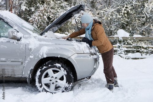 Photo: Woman standing in snow checking underneath carճ hood Woman standing in snow checking underneath carճ hood