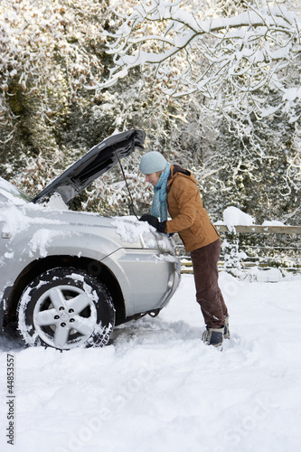 Photo: Woman standing in snow checking underneath carճ hood Woman standing in snow checking underneath carճ hood