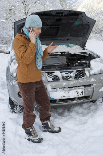 Photo: Woman standing in snow checking underneath carճ hood and talking on cell phone Woman standing in snow checking underneath carճ hood and talking on cell phone