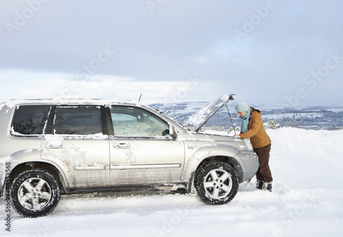 Photo: Woman standing in snow checking underneath carճ hood Woman standing in snow checking underneath carճ hood