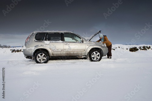 Photo: Woman standing in snow checking underneath carճ hood Woman standing in snow checking underneath carճ hood