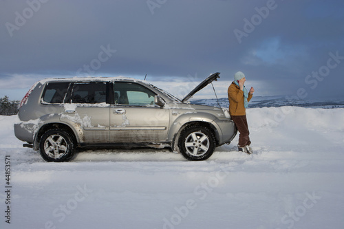 Photo: Woman standing in snow checking underneath carճ hood and talking on cell phone Woman standing in snow checking underneath carճ hood and talking on cell phone