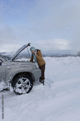Photo: Woman standing in snow checking underneath carճ hood talking on cell phone Woman standing in snow checking underneath carճ hood talking on cell phone