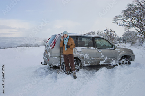 Photo: Woman standing in snow with skidded car talking on cell phone Woman standing in snow with skidded car talking on cell phone
