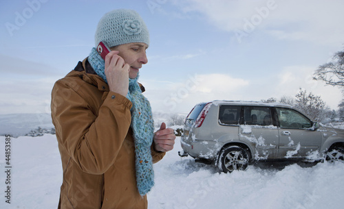 Photo: Woman standing in snow with skidded car talking on cell phone Woman standing in snow with skidded car talking on cell phone