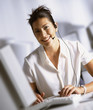 Smiling businesswoman in headset typing on computer