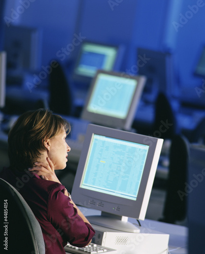 Photo: Businesswoman sitting at desk working late and rubbing neck Businesswoman sitting at desk working late and rubbing neck