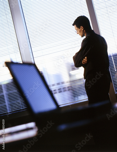Photo: Businessman with arms crossed looking out office window Businessman with arms crossed looking out office window
