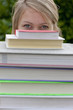 Close up of young woman peering from behind stack of textbooks