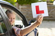 Photo: Portrait of smiling young woman driving car and holding learnerճ permit sticker out window Portrait of smiling young woman driving car and holding learnerճ permit sticker out window