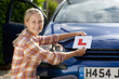 Portrait of smiling young woman attaching learnerճ permit sticker to car