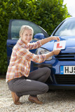 Photo: Portrait of smiling young woman attaching learnerճ permit sticker to hood of car Portrait of smiling young woman attaching learnerճ permit sticker to hood of car