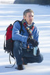 Man crouching in snow with backpack and insulated drink container