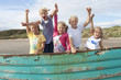 Portrait of enthusiastic boy and girls with arms raised in boat on beach