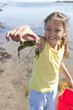 Smiling girl holding small crab on sunny beach