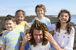 Portrait of smiling kids holding seaweed over man's head on sunny beach