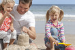 Father and daughters making sandcastle on sunny beach
