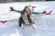 Portrait of smiling mother and daughter laying on sled with arms outstretched in snow
