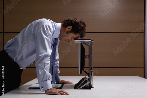 Photo: Frustrated businessman leaning on computer in office Frustrated businessman leaning on computer in office