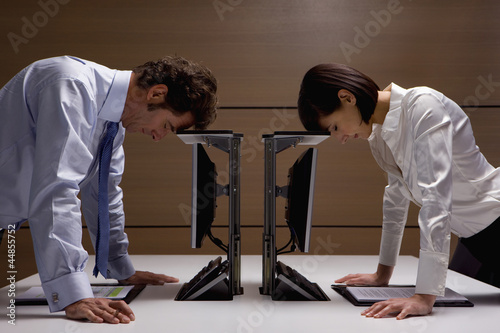Photo: Businessman and businesswoman leaning on computers in office Businessman and businesswoman leaning on computers in office