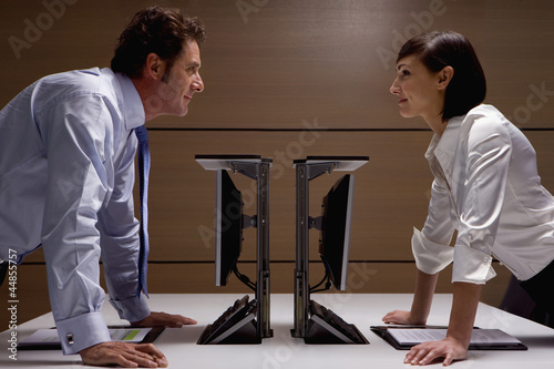 Photo: Smiling businessman and businesswoman leaning on desks face to face Smiling businessman and businesswoman leaning on desks face to face
