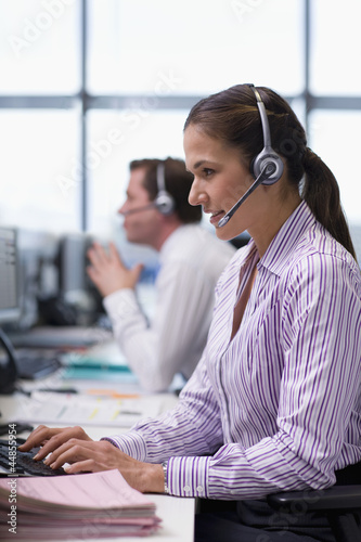 Photo: Businesswoman wearing headset and typing on computer keyboard in office Businesswoman wearing headset and typing on computer keyboard in office