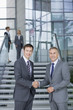 Portrait of smiling businessmen in suits shaking hands at steps in lobby