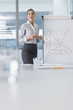 Photo: Portrait of smiling businesswoman standing at chart in conference room Portrait of smiling businesswoman standing at chart in conference room
