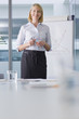 Photo: Portrait of smiling businesswoman standing at chart in conference room Portrait of smiling businesswoman standing at chart in conference room