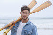 Portrait of young man holding oars on beach