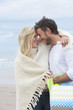 Smiling couple with blanket and basket hugging face to face on beach