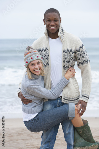Photo: Portrait of young woman hanging from boyfriend on beach Portrait of young woman hanging from boyfriend on beach