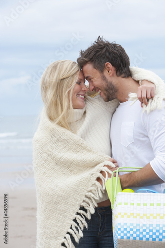 Photo: Smiling couple with blanket and basket hugging face to face on beach Smiling couple with blanket and basket hugging face to face on beach