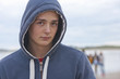 Portrait of serious teenage boy in hoody on beach with friends in background