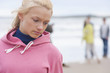 Pensive teenage girl on beach with friends in background