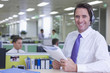 Portrait of smiling businessman wearing headset and reviewing report in office