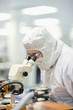 Photo: Scientist in clean suit examining silicon wafer in telescope in laboratory Scientist in clean suit examining silicon wafer in telescope in laboratory