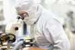 Photo: Scientist in clean suit examining silicon wafer in telescope in laboratory Scientist in clean suit examining silicon wafer in telescope in laboratory