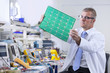Engineer examining printed circuit board at electrical test bench